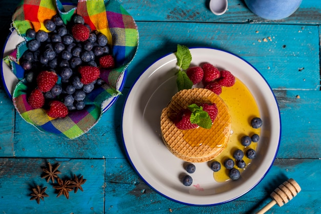 Desayuno holandés waffle con frambuesa, arándanos y miel sobre fondo de madera azul. Imagen aislada toma aérea Concepto de desayuno.