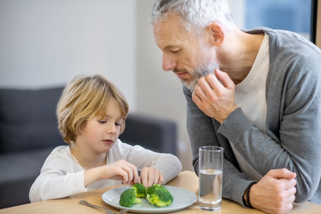 Desayuno. Hombre maduro tratando de hacer que su hijo coma sano mientras el niño parece infeliz