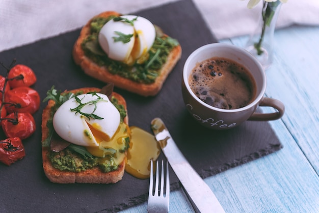 Desayuno con huevo escalfado sobre paleta de aguacate y albahaca y una taza de café