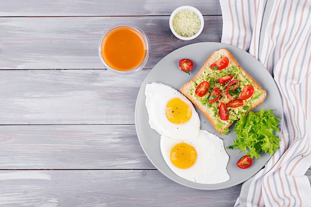 Desayuno. Huevo frito, ensalada de verduras y un sándwich de aguacate a la parrilla sobre un fondo gris. Vista superior