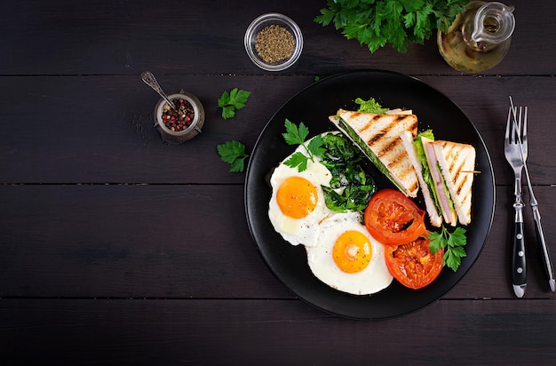 Desayuno huevo frito espinacas tomates y sándwich de club en el plato Vista superior espacio de copia