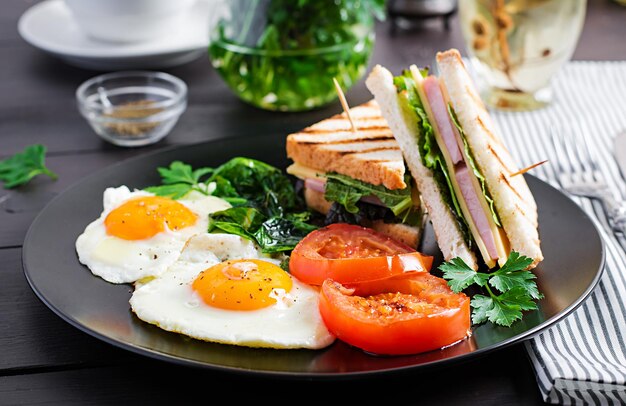 Desayuno huevo frito, espinacas, tomates y sándwich en el plato.