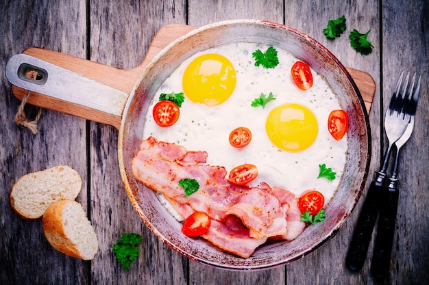 Desayuno con huevos fritos tocino tomates y perejil en mesa rústica