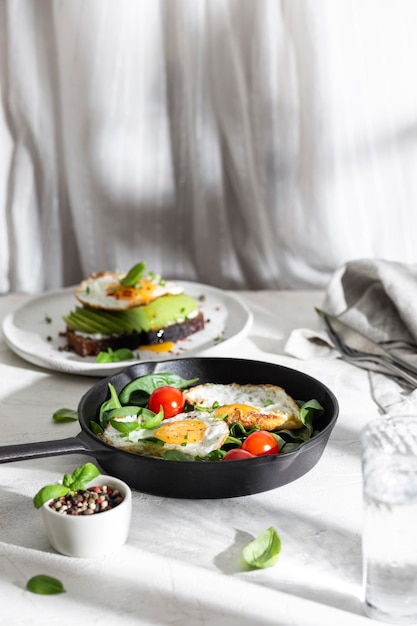 Desayuno con huevos fritos y verduras en una sartén.