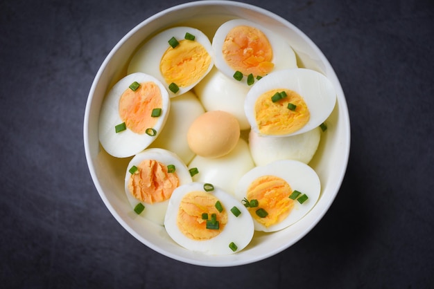 Desayuno de huevos, menú de huevos frescos, huevos cocidos en un bol decorado con hojas de cebollas verdes frescas picadas sobre fondo oscuro, ingredientes de yemas de huevo cortados a la mitad para cocinar un concepto de alimentación saludable