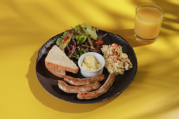 Desayuno con huevos revueltos y salchichas a la barbacoa con verduras y tostadas sobre un fondo amarillo con la sombra de una palmera