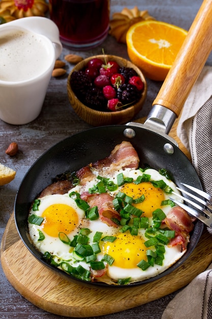 Desayuno huevos revueltos con tocino, café, bayas, galletas, nueces y jugo en la superficie de la mesa oscura