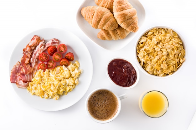 Desayuno con huevos revueltos, tocino, tomate, café, jugo de naranja, croissant y hojuelas de maíz.