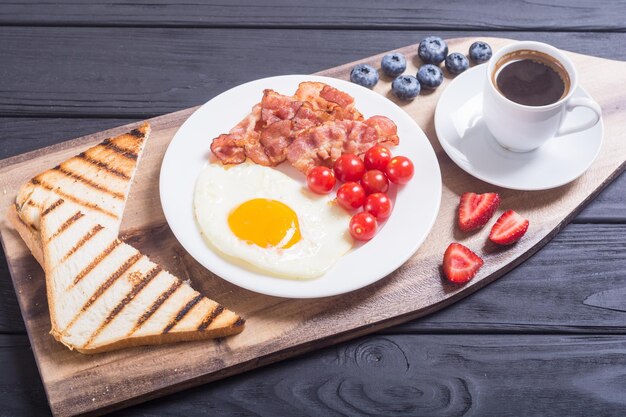 Desayuno con huevos, tocino, tomates, café y bayas.