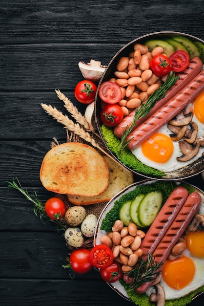 Desayuno inglés completo con huevos fritos, salchichas, frijoles, tostadas y café sobre fondo de espacio de copia Sobre un fondo de madera negra