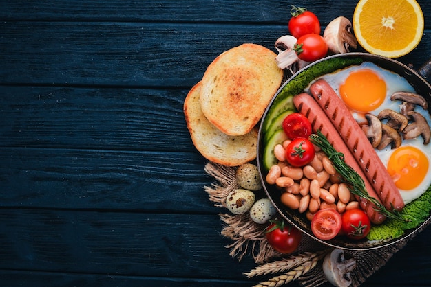 Desayuno inglés completo con huevos fritos, salchichas, frijoles, tostadas y café sobre fondo de espacio de copia Sobre un fondo de madera negra