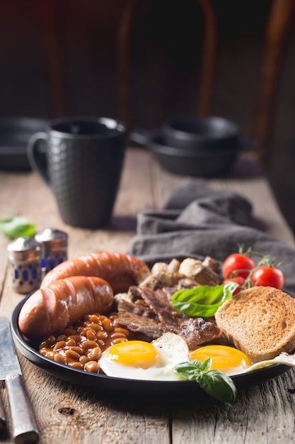 Foto desayuno inglés completo con huevos fritos, salchichas, tocino, frijoles, tostadas y tomates en madera rústica