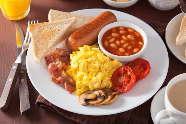 Desayuno inglés completo con huevos revueltos, tocino, salchichas, frijoles y tomate.