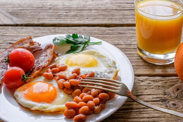 Desayuno inglés completo con huevos tocino frijoles tomates y jugo de naranja en un plato con tenedor