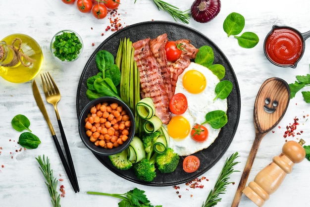 Desayuno inglés garbanzos aguacates huevos revueltos tocino verduras en un plato de piedra negra Vista superior Espacio libre para texto