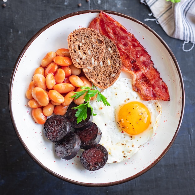 Desayuno inglés huevo frito morcilla morcilla pan de cereales frijoles tocino huevos revueltos