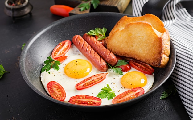 Desayuno inglés: huevo frito, tomates, salchichas y tostadas. Vista superior