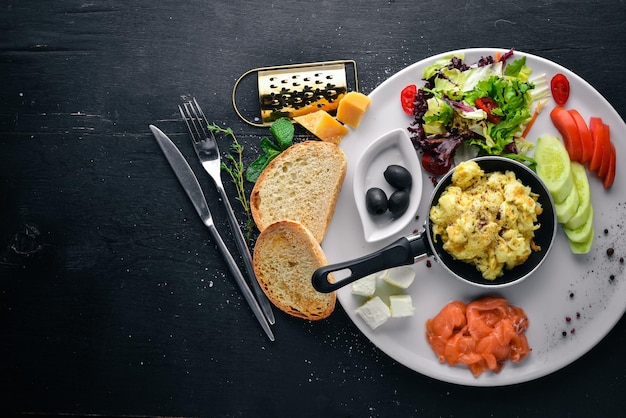 Desayuno inglés Huevos fritos Salmón Aceitunas Nueces Verduras y frutos secos Vista superior Espacio libre para texto Sobre un fondo de madera