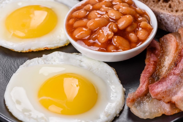 Desayuno inglés con huevos fritos tocino frijoles tomates especias y hierbas