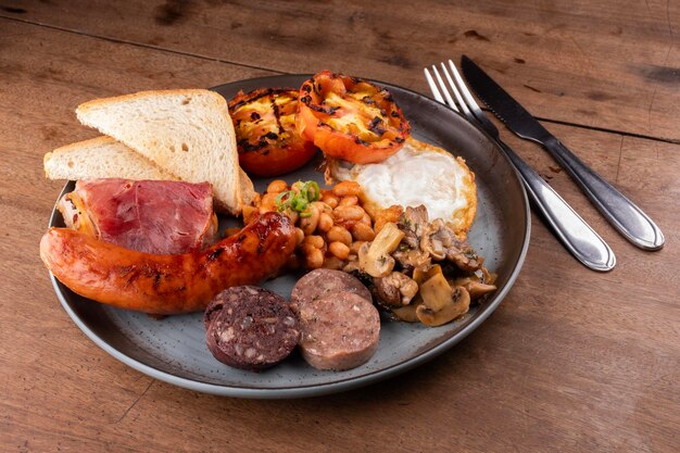 Foto desayuno: inglés, irlandés, británico, con muchas proteínas, frijoles dulces, salchichas, tocino, huevo, setas, pudín blanco y negro.