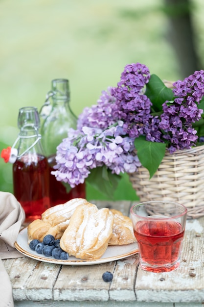 Desayuno en el jardín: canutillos, taza de café, cafetera, flores de color lila en una cesta.