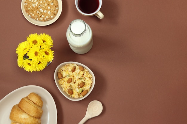 Foto desayuno con leche, muesli y flores sobre fondo marrón