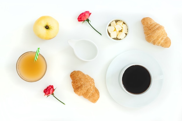 Desayuno por la mañana café y croissant, mantequilla, jugo de naranja y flores sobre fondo blanco.