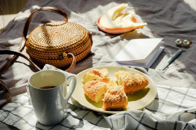 Desayuno matutino en la cama sobre una manta con fruta de té y bolsa de mimbre de pastel y cuaderno de color verde claro