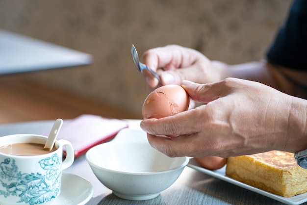 Desayuno matutino Hombre rompiendo la cáscara de un huevo hervido con una cuchara