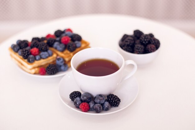 Desayuno matutino con taza de té, gofres y bayas.