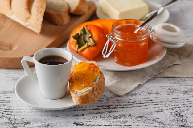 Desayuno con mermelada de frutas de caqui y café en la mesa de madera