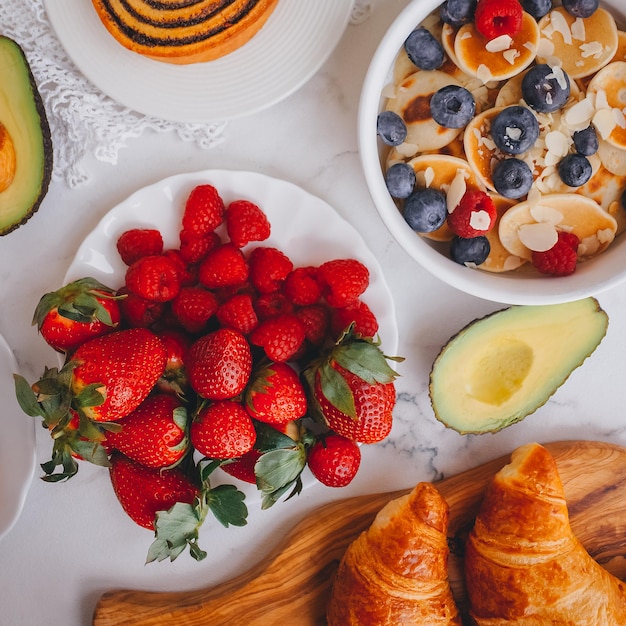 Foto desayuno, mini crepes con fresas, croissants y aguacate, deliciosa comida de verano, vista superior sobre una espalda de mármol