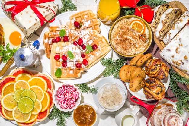 Desayuno navideño festivo o mesa de brunch con comidas tradicionales: tortitas, gofres belgas, huevos fritos, croissant, galletas robadas con jugo de naranja y café, canela, arroz, gachas de avena.