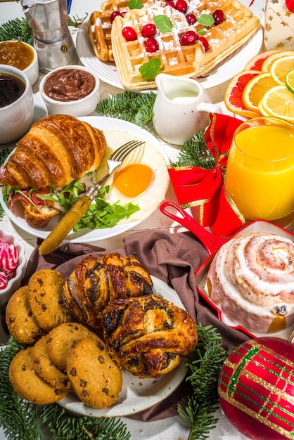 Desayuno navideño festivo o mesa de brunch con comidas tradicionales: tortitas, gofres belgas, huevos fritos, croissant, galletas robadas con jugo de naranja y café, canela, arroz, gachas de avena.