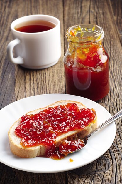 Desayuno con pan, mermelada y taza de té en la mesa de madera antigua