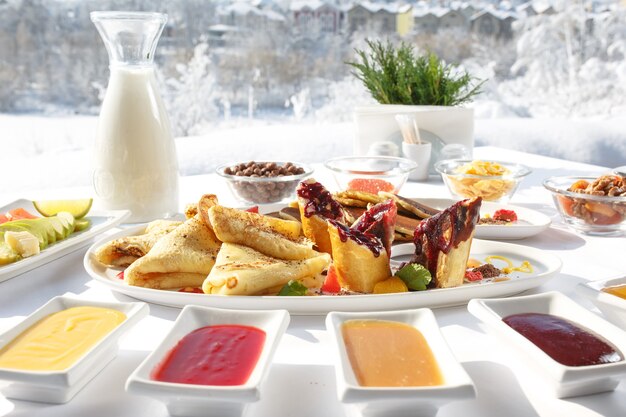 Desayuno de panqueques de invierno en la terraza afuera del restaurante en el fondo de nieve Panqueques, fruta, jugo y café