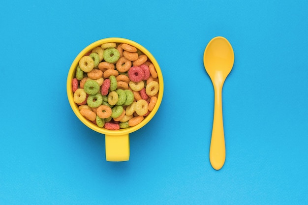 Un desayuno preparado de anillos de maíz multicolores y una cuchara sobre un fondo azul Lay Flat