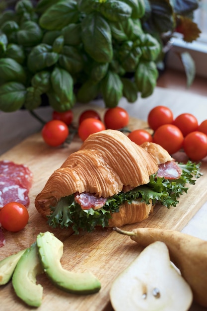 Desayuno de primer plano con sándwich de croissant fresco casero con jamón, aguacate, tomate y lechuga