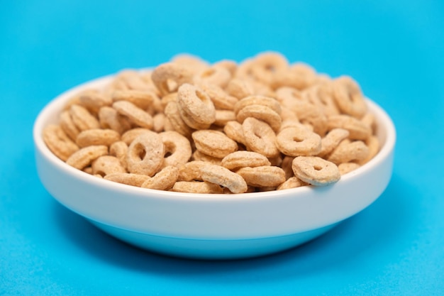 Desayuno rápido de cereales en forma de anillos en un plato de fondo azul