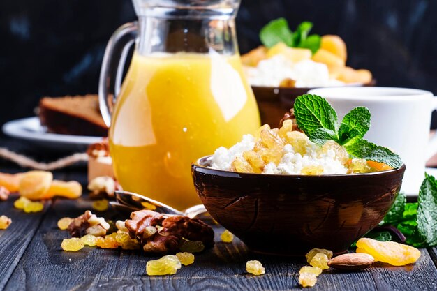 Desayuno con requesón casero, jugo recién exprimido, nueces y frutos secos, enfoque selectivo de fondo oscuro