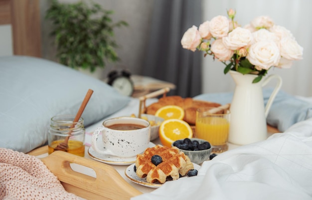 Desayuno romántico con café, gofres, jugo de naranja y rosas.