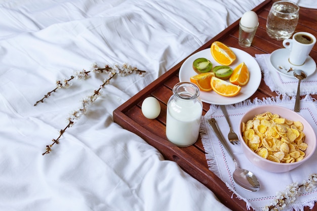 Desayuno romántico en la cama con flores de primavera. Luz de la ventana, copia espacio