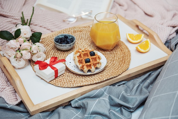 Desayuno romántico con gofres, jugo de naranja y flores de rosas y caja de regalo.