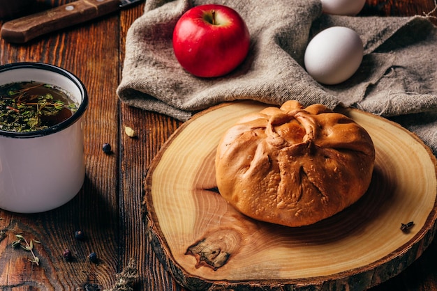 Desayuno rústico con elesh de pastelería tártara tradicional, té de hierbas en una taza de metal, manzana y huevos cocidos sobre una superficie de madera oscura