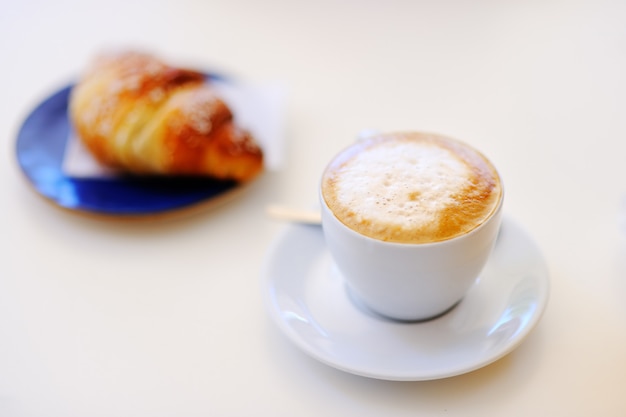 Desayuno sabroso en una cafetería italiana de la calle: taza de café y croissant en una mesa blanca