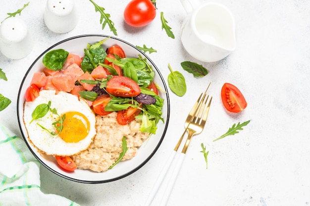 Desayuno sabroso Gachas de avena con huevo de salmón salado y ensalada fresca Vista superior sobre mesa blanca con espacio para copiar