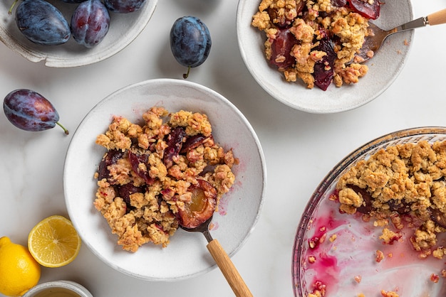 Desayuno sabroso. Pastel de frutas de ciruela en platos con cucharas y una taza de té con limón en la mesa de mármol blanco