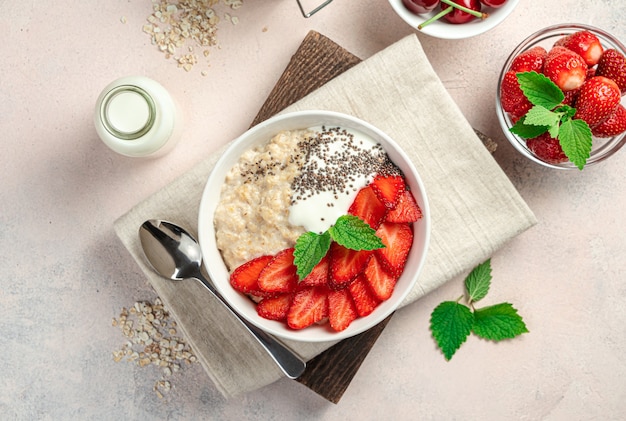 Desayuno saludable con avena con fresas y semillas de chía sobre un fondo rosa