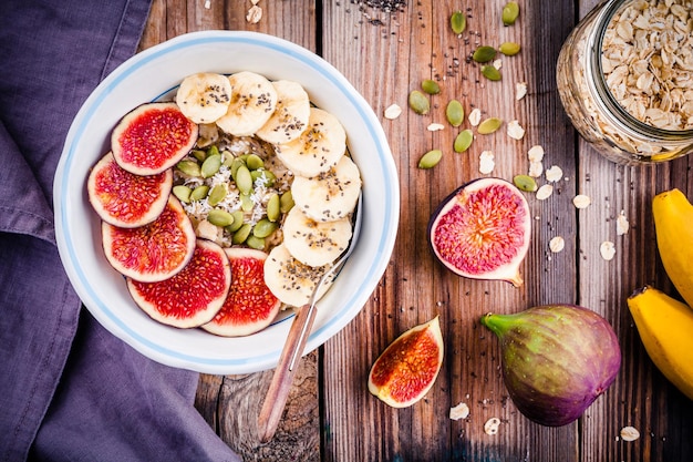 Desayuno saludable avena con higos frescos plátanos semillas de calabaza coco y semillas de chía en mesa de madera