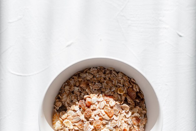 Desayuno saludable con avena, nueces y frutos secos sobre una mesa blanca con luces solares.